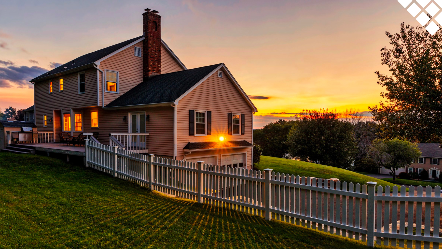 Sunsetting on landscape of home with porch, chimney and picket fence on beautiful green lawn